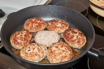 Beef and pork meat patties are roasted in a pan on a gray-colored electric stove in the kitchen at home. homemade delicious food. cooking at home. hearty lunch