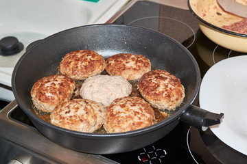 Beef and pork meat patties are roasted in a pan on a gray-colored electric stove in the kitchen at home. homemade delicious food. cooking at home. hearty dinner