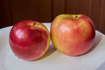 Two red juicy apples lie side by side on a white plate. fruits and vegetables. vitamin c. energy of nature