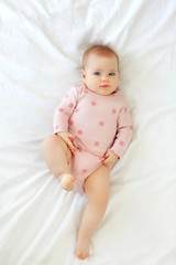 A charming blue-eyed baby with a funny hairstyle 9 months lies in bed in a pink body