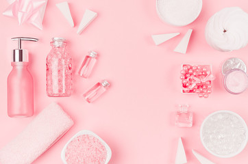 Cosmetic products and accessories in pink color - cream, bath salt, essential oil, soap, towel, sponge, pearls, bottles, bowl on pink background, copy space.