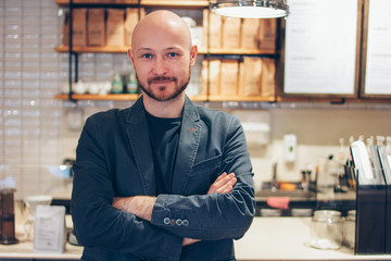 Portrait of attractive adult successful bald bearded man in suit on cafe coffee house background