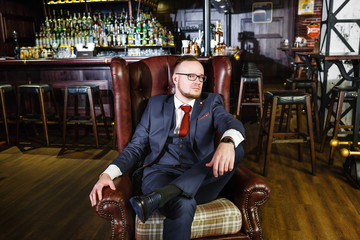 stylish man in a suit sits in a chair in a pub