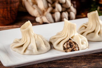 The concept of Georgian cuisine. Khinkali from white dough with mushrooms. Serving dishes in Georgian restaurant on a white plate, on a wooden table. Background image. copy space