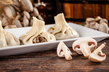The concept of Georgian cuisine. Khinkali from white dough with mushrooms. Serving dishes in Georgian restaurant on a white plate, on a wooden table. Background image. copy space