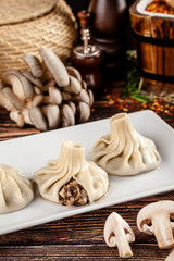 The concept of Georgian cuisine. Khinkali from white dough with mushrooms. Serving dishes in Georgian restaurant on a white plate, on a wooden table. Background image. copy space