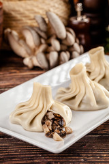The concept of Georgian cuisine. Khinkali from white dough with mushrooms. Serving dishes in Georgian restaurant on a white plate, on a wooden table. Background image. copy space