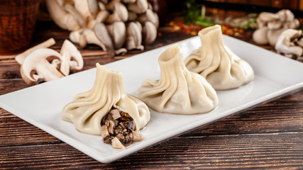 Fototapeta na wymiar The concept of Georgian cuisine. Khinkali from white dough with mushrooms. Serving dishes in Georgian restaurant on a white plate, on a wooden table. Background image. copy space