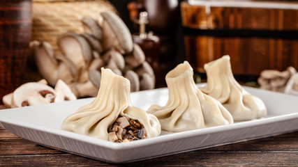 Fototapeta na wymiar The concept of Georgian cuisine. Khinkali from white dough with mushrooms. Serving dishes in Georgian restaurant on a white plate, on a wooden table. Background image. copy space