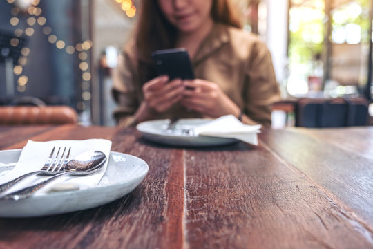 Closeup image of a beautiful woman holding , using and looking at smart phone while having a meal in restaurant