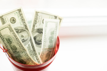 Dollar bills in red pail. on white window.light background. place for text. top view. a lot of money