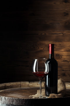 Bottle and glass of red wine on wooden barrel shot with dark wooden background