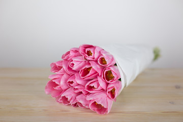A bouquet of pink tulips in wrapping paper on a wooden table. Close-up