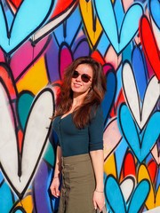 Brunette girl with long hair stands on the background of graffiti with colorful hearts