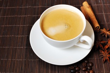 Cup of hot coffee with cinnamon and anise star decoration on brown wooden background. Top table