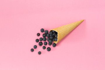 Freshly blueberries in an ice cream cone on a pink background. Blueberry explosion. Summer refreshment concept. Flat lay, top view. Natural Organic Food Style.