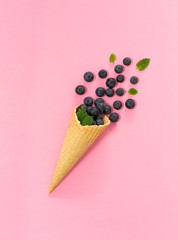 Freshly blueberries in an ice cream cone on a pink background. Blueberry explosion. Summer refreshment concept. Flat lay, top view. Natural Organic Food Style.