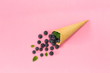 Freshly blueberries in an ice cream cone on a pink background. Blueberry explosion. Summer refreshment concept. Flat lay, top view. Natural Organic Food Style.