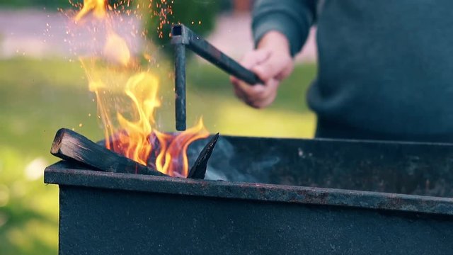 CU, Slow motion: man pushes the burning firewood in brazier with poker.