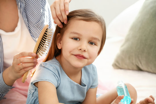 Young Mother Brushing Hair Of Her Cute Little Daughter At Home