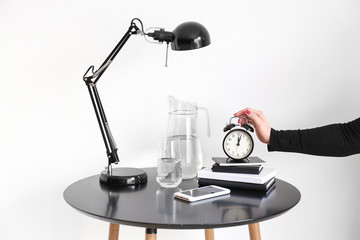Woman turning off alarm clock on table against white background