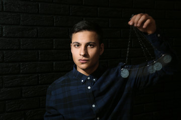 Male hypnotist with swinging pendulum on dark background