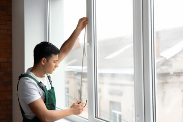 Male worker taking measurements of window in flat