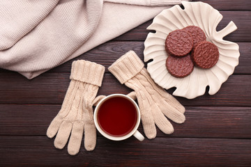 Cup of hot tea, warm gloves and tasty cookies on wooden background