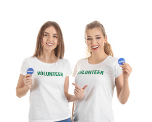 Young female volunteers with badges on white background