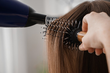 Hairdresser with blow drier brushing long hair of young woman in salon, closeup