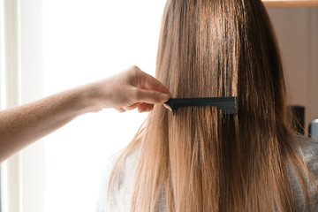 Hairdresser combing long hair of young woman in salon