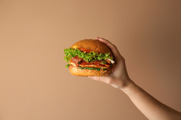 Female hand with tasty burger on color background