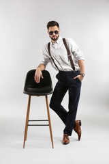 Fashionable young man with chair on light background