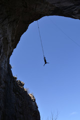 Silhouette of a man jumping in a cave hanging high on a cord. Upwards view. Bungee jump in Pohodna...