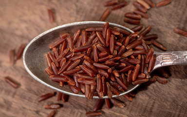 Vintage spoon full of red rice on rustic wooden background