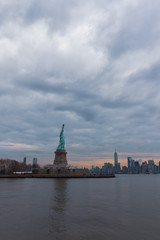 View of New York City skyline and Statue of Liberty with dramatic sky at dusk, New York, USA