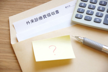 封筒に入った病院の医療費の領収書と電卓とペンとはてなマークが書かれた付箋紙