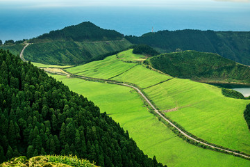 Fototapeta premium Aerial view on scenic landscape of volcanic lake Sete Cidades and green fields around it. Special shape of ground. Atlantic ocean on background. Azores islands, Sao Miguel, Portugal.
