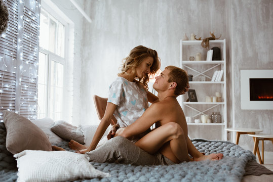 Couple in the bedroom on the bed in the bedroom. A blonde girl in pajamas, a guy with a naked torso. Love and hugs. A beautiful couple. New Year's interior. Christmas time. A blanket of large mating.