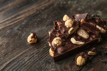 Pieces of tasty dark chocolate with nuts on wooden background