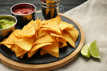 Board with tasty nachos and sauces on table