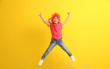 Fototapeta na wymiar Funny little girl in wig jumping against color background