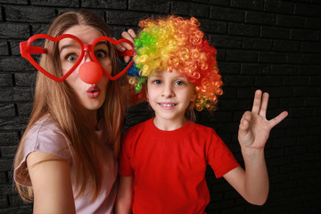 Woman and little girl in funny disguise on dark background. April fools' day celebration