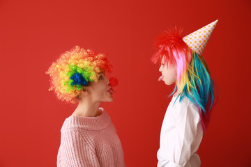 Woman and little girl in funny disguise on color background. April fools' day celebration