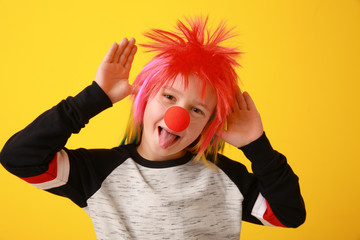Funny little boy with clown nose and wig on color background. April fools' day celebration