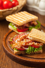 Toasted sandwich with bacon, tomato, cucumber and lettuce.
