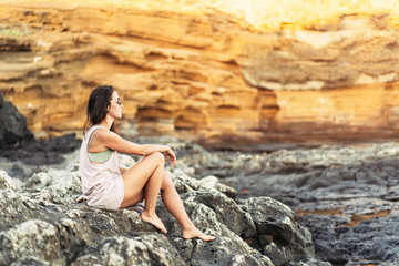 Pretty long hair brunette tourist girl relaxing on the stones near sea.