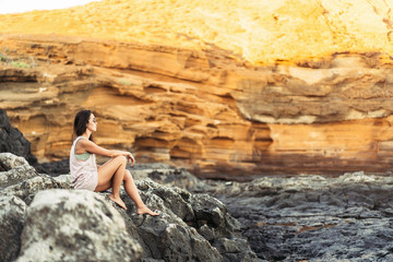 Pretty long hair brunette tourist girl relaxing on the stones near sea.