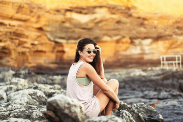 Pretty long hair brunette tourist girl relaxing on the stones near sea.