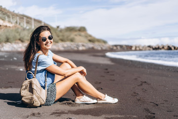 Fototapeta na wymiar Pretty brunette long hair girl relaxing on the beach with black sand near sea